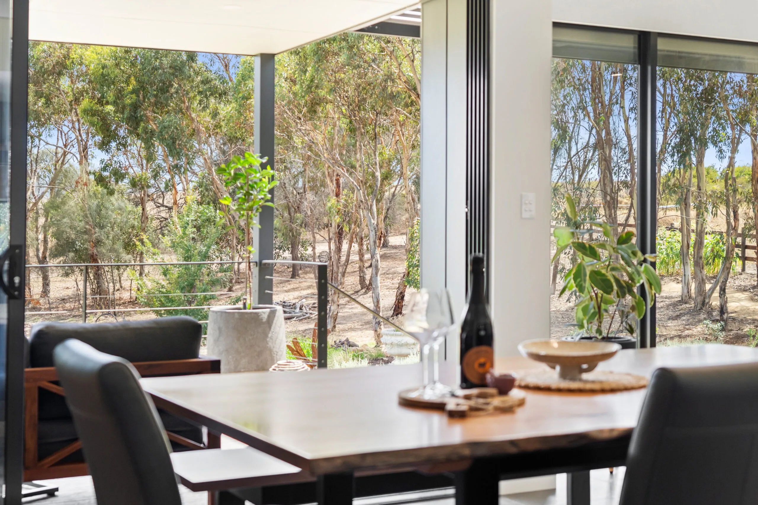 Dining area of a sustainable Magor Builders home opening through wide glass sliding doors to a gum-treed bush outlook on the Fleurieu Peninsula.