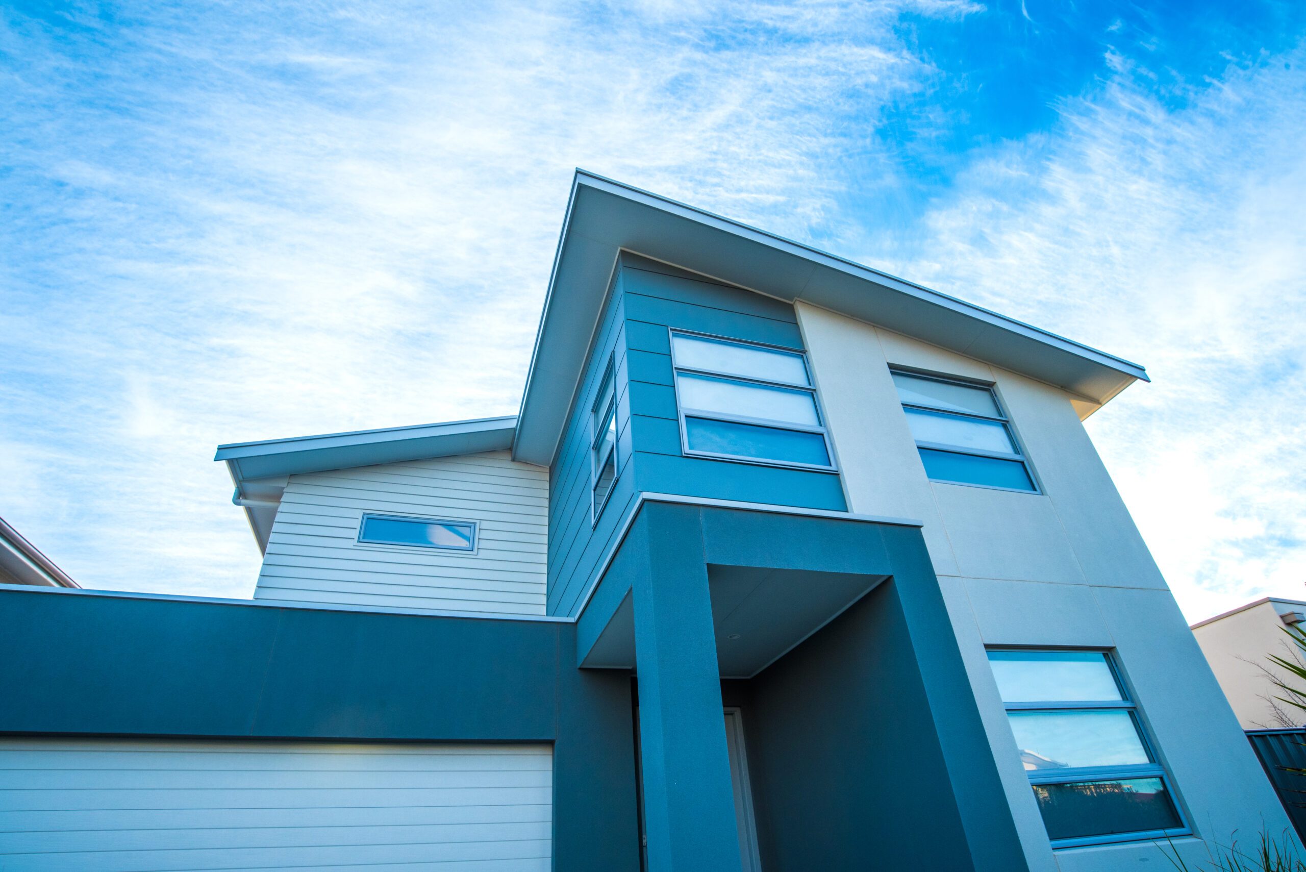 Front elevation of the Cormorant, a two-storey Magor Builders home with a skillion roof, weatherboard and render facade, shot against a blue sky.