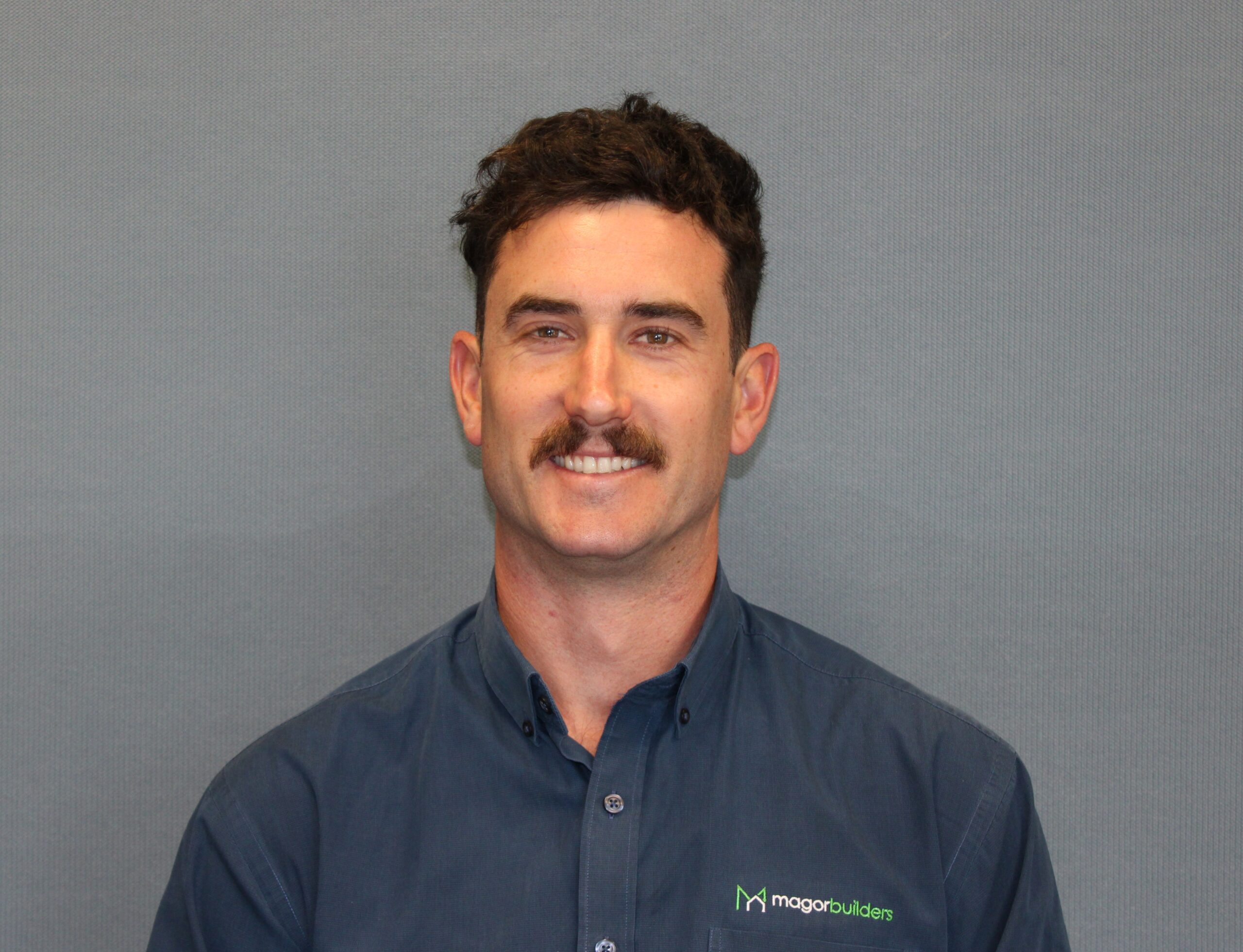 Portrait of Liam Magor of Magor Builders, smiling in a navy Magor Builders shirt.