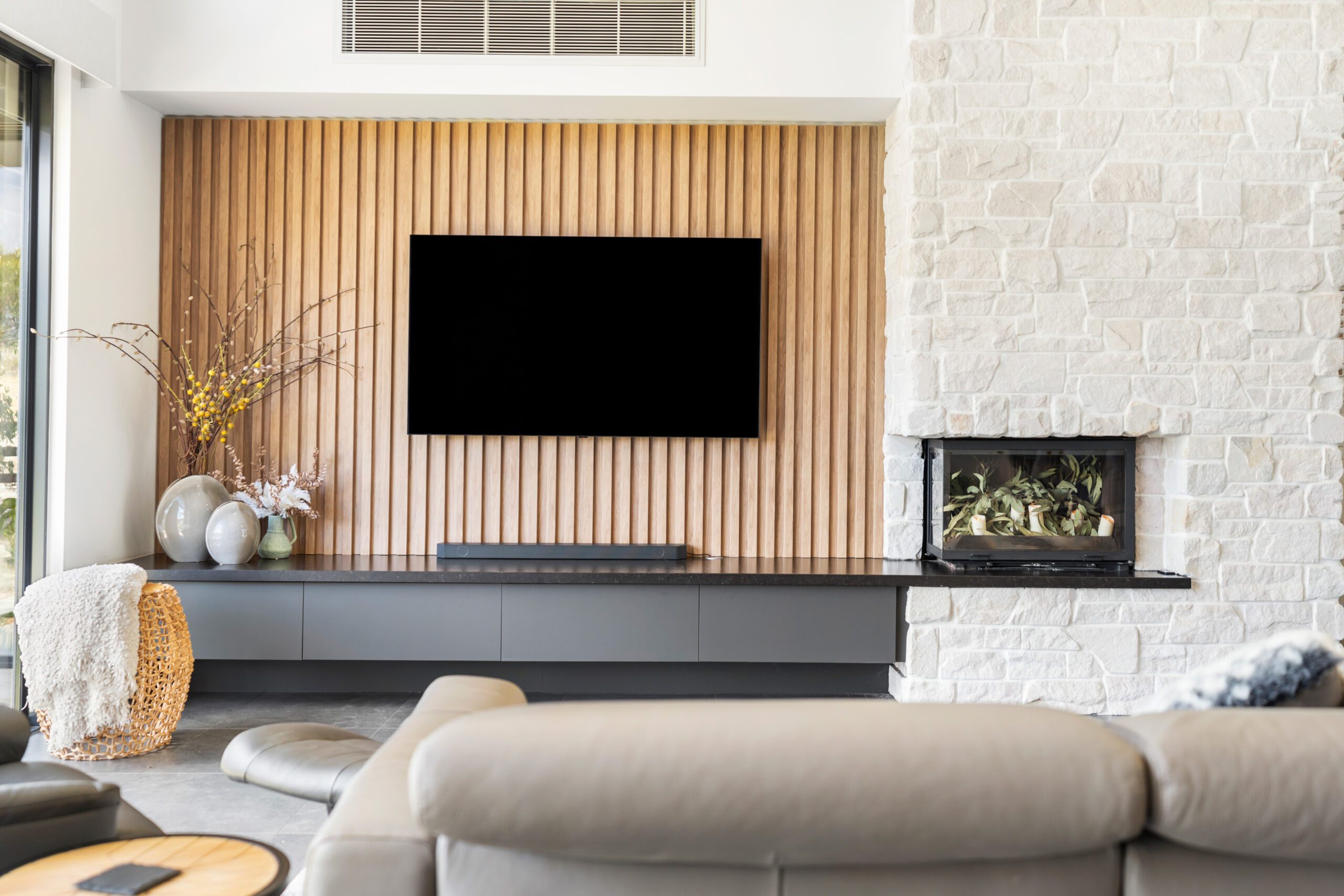 Living room in a Magor Builders home with a timber batten TV wall, a white natural stone fireplace with an inbuilt combustion fire and a leather lounge.